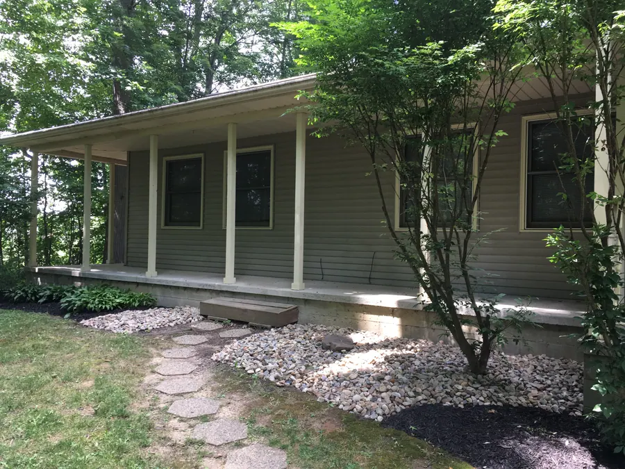 Covered townhome porch beside trees and landscaped stone beds