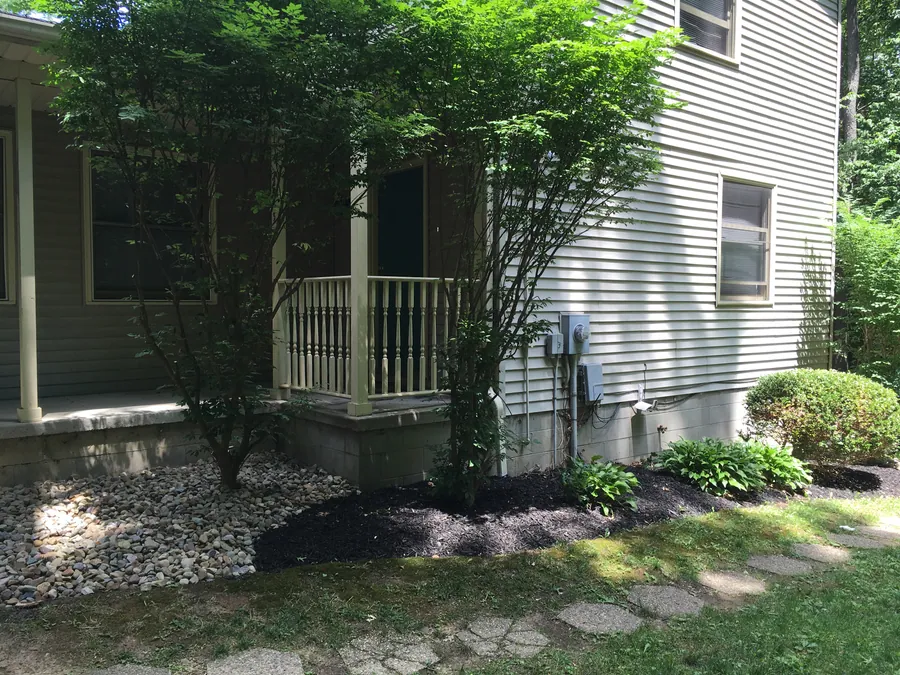 Shaded porch beside mature trees, shrubs and a landscaped stone bed
